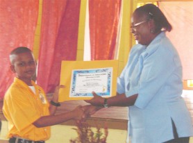 DCEO Dev. Donna Chapman presents certificates to a West Ruimveldt Primary student who received the certificates on behalf of his school.