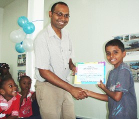 GWI Director of Finance, Ravin Paltoo presents a young participant with a certificate of participation, while others look on.