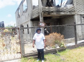 I will build again: Victorine Ifill stands in front of the burnt out structure that was once her home.