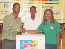 Courts Inc. Public Relations Officer Pernell Cummings (left) hands over the refridgerator to Abigail McDonald in support of the GASP’s raffle. At centre is Leon Belony of the scrabble association.