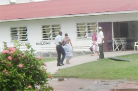 The tortured teen (second, left) with a sheet wrapped around his waist being escorted into the West Demerara Regional Hospital by a policeman yesterday. At right is the hospital security guard. The teen’s mother Shirley Thomas (second, right) walks ahead into the hospital. (Photo by Zoisa Fraser) 