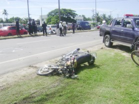 Kenrick Mitchell’s motorcycle lies on the parapet at the scene of the accident as police officers, in background, carry out investigations yesterday.