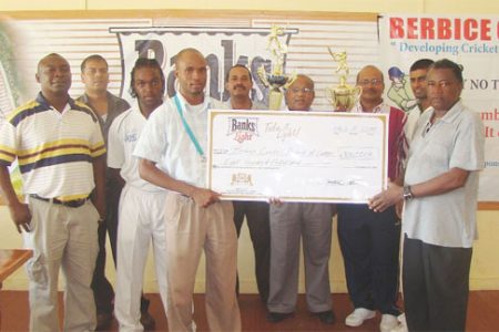 Banks DIH Brand Management Trainee Ian De Barros  presents a replica of the sponsorship cheque to Berbice Cricket Board President Keith Foster while officials of Banks DIH and the BCB look on.