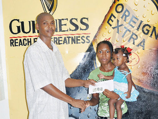 Lyall Gittens (left) makes the donation to Shenise Lopes who holds her daughter Amayah Lopes. (Orlando Charles Photo)