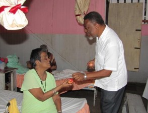 Prime Minister Sam Hinds shares an apple to a resident of the Dharm Shala (GINA photo)