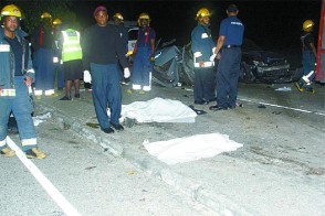 Fire officers stand around the bodies of two of the accident victims, who were killed on Friday evening on the Churchill-Roosevelt Highway in Arouca. (Trinidad Guardian photo)