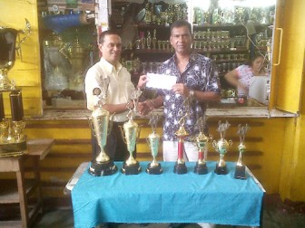 Treasurer of the Guyana Chess Federation, Shiv Nandalall (left), receives the sponsorship cheque and trophies from Managing Director of the Trophy Stall, Ramesh Sunich yesterday at the Trophy Stall’s Bourda Market location (Floyd Christie photo).