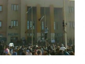 People climb flag poles in front of a building purported to be the internal security headquarters in Libya's second city of Benghazi in this still grab taken from video uploaded February 20, 2011. REUTERS/Youtube via Reuters TV