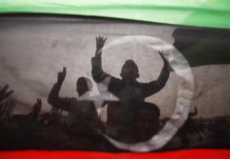 Protesters are seen through a Kingdom of Libya flag during celebrations after a U.N. resolution authorizing a "no-fly" zone, in Tobruk, east of Tripoli, March 18, 2011. REUTERS/Suhaib Salem