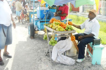 Fruit vendor Maxwell Bridgemohan  interacts with a customer at his stand at the  Anna Regina market recently.