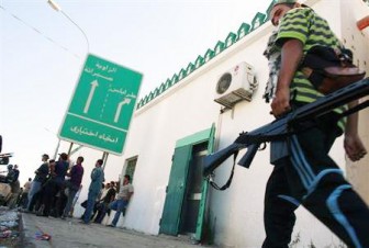 Rebel fighters wait at a checkpoint near a sign pointing to Tripoli in the coastal town of Zawiyah, 50 km (30 miles) west of Tripoli, August 14, 2011. REUTERS/Bob Strong