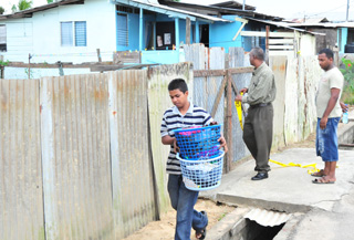 Rocky Ramsundar (with basket of clothes) leaves the house where his mother Sohanie was killed yesterday at Teelucksingh Street East, California. (Trinidad Express photo)