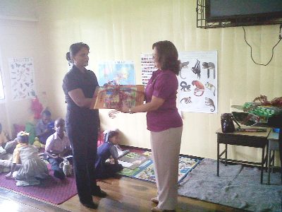 Head teacher of East La Penitence Primary School, Sherron Howard, (left) receives a donation from Scotiabank Guyana Country Manager, Amanda St Aubyn (right) in the reading room of the East La Penitence Primary. Children can be seen in the background taking advantage of the donation.
