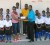 Tucville Primary Football team flanks Teacher Donette Munroe-Liverpool (collecting envelope from Carlos Bernard) and Marlan Cole and Coach Terrence Clark standing in back row. 