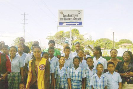 Staff and children of the school and members of the Lions Club stand in front of the sign