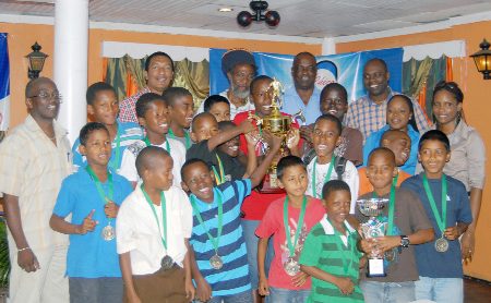 Chico Under-13 football tourney winners Soesdyke Primary School smile broadly as they display their trophy and medals while K&S directors Kashif Mohammed and Aubrey Major  and other supporters look on.