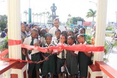 Minister of Culture Youth & Sport Dr Frank Anthony (back, centre) looks on approvingly as St Sidwell’s Primary School pupil Tanya Schultz, assisted by several of her peers, cuts the ribbon to declare the information centre at the 1763 Monument open. (Photo by Arian Brown)