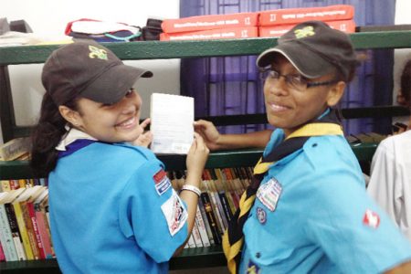 Two girl scouts smile as they display a book in the new library and computer room the Scout Association opened on Woolford Avenue.
