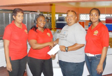 Troy Yhip, the Youth Development Officer (YDO) and tournament coordinator of the GRFU, accepts the sponsorship cheque from one of Hamson’s managers, Emilia Nwankwo to aid with the GRFU/Hamson’s Under-14 Mashramani tournament as other representatives of the company looks on. (Orlando Charles photo) 