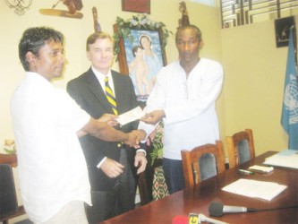  Sahaboob Yassin (left) hands over the cheque for the magazine publication to SFCD Head Alex Foster. Looking on (centre) is US Ambassador Brent Hardt