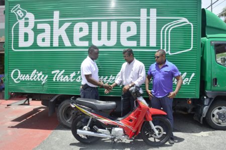 Jacob Nanan (centre) hands over the Jialing 110cc motorcycle to Aubrey Major Jr. in front of Bakewell’s Albert Street outlet as Kenrick Noel, a New Era Entertainment Director looks on. 