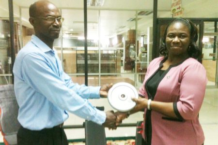 Lyndon France, head of the Technical Department of Buxton United receives a gym plate from Shonell Yarde, Manager of the Gym and Home Appliances Department as a symbolic gesture of the donation yesterday morning at the Gafsons Industries Limited, Huston.