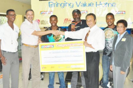 Courts Managing Director Clyde De Haas hands over the cheque to Peter Abdool, third from right. Others in picture are from left, PRO Kester Abrams, Clive Atwell, Howard Eastman, boxer Kishan Simon and Pamela Humphrey.
