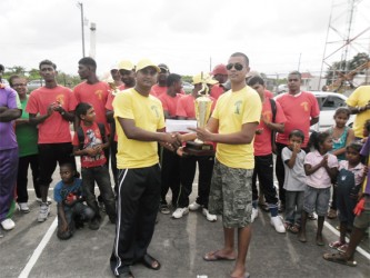 Ryan Sankar (right) of Universal DVD Club, hands over the victorious trophy and cash prize to Universal DVD Club Titans’ skipper Balram Samaroo. In the background are members of the Blairmont Number 1 team, who placed third. 