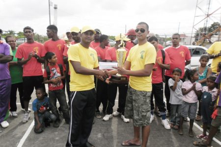 Ryan Sankar (right) of Universal DVD Club, hands over the victorious trophy and cash prize to Universal DVD Club Titans’ skipper Balram Samaroo. In the background are members of the Blairmont Number 1 team, who placed third.

