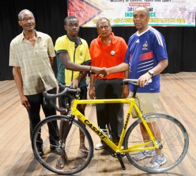 USA-based Guyanese Aubrey Gordon (right) presents Shaquille Agard with a new racing cycle in the presence of national coach Hassan Mohamed (second right) and race official, William Howard.   