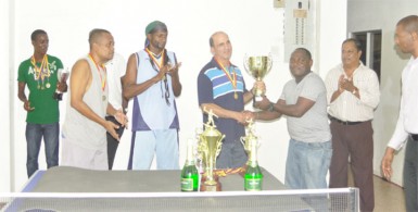 NP Electronics skipper Michael Vieira receives the team’s first place trophy from a member of the Guyana Table Tennis Association. 