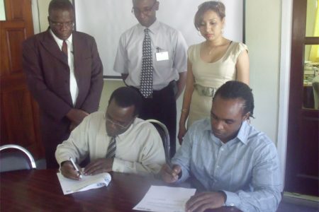 The signing of a Memorandum of Understanding between Habitat for Humanity Guyana Inc. and the Adventist Development and Relief Agency Guyana (ADRA) on Thursday to formalise a partnership to develop underprivileged communities. Seated (left to right) are Dennis Hamilton, Director of ADRA and Rawle Small, National Director of HfHG, while standing are representatives of the two organisations. (Habitat for Humanity Guyana Inc photo)