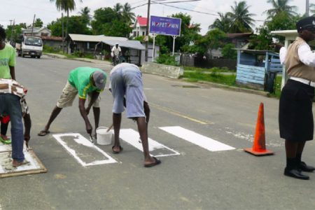 A police officer directs traffic as Joseph (left) and others paint the crossing at Hopetown yesterday morning