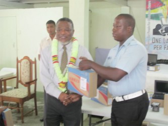 Prime Minister Samuel Hinds hands over one of the 1,050 computers available in the final round of distribution for Region 4 to Officer Ronald Thomas at the Zoar Congregation Church at Plaisance, East Coast Demerara. 