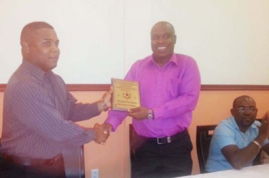 GFF President Christopher Matthias receives a plaque from GFA President Vernon Burnett while GFF Vice-President of Administration Rawlston Adams looks on.