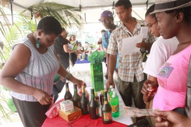 Bernice Trotz readies samples of the Phoenix Enterprise’s coconut and fruit wine during the New GMC’s first Coconut Exposition yesterday. (Photo by Arian Browne) 