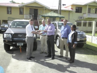 A representative of the German Development Bank (left) making the symbolic handover of the two vehicles to Natural Resources Minister, Robert Persaud. 