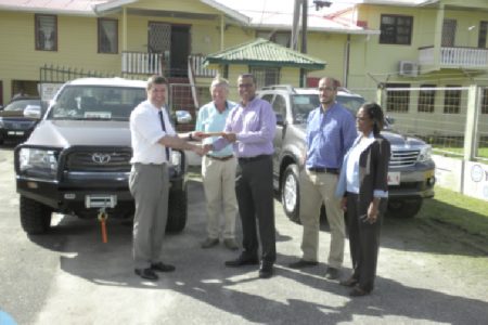 A representative of the German Development Bank (left) making the symbolic handover of the two vehicles to Natural Resources Minister, Robert Persaud.
