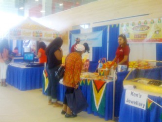An attendant at Beharry booth smiles as two visitors look at locally-produced goods on display at the Guyana Independence Festival held in Canada. (Guyana Tourism Authority Photo)  