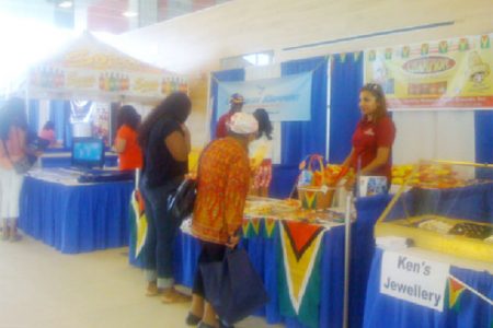 An attendant at Beharry booth smiles as two visitors look at locally-produced goods on display at the Guyana Independence Festival held in Canada. (Guyana Tourism Authority Photo)
