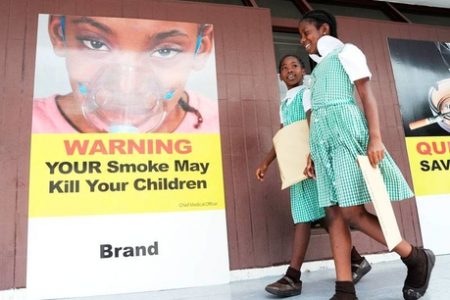 Students of St George's Girls' Primary and Infant School walk by a sign placed near the entrance to Gordon House by the Ministry of Health yesterday. The health ministry, in collaboration with the Jamaica Cancer Society and the National Council on Drug Abuse, set up an exhibition outside Parliament with a focus on cancer and the cessation of tobacco use to coincide with a Sectoral Debate contribution from Health Minister Dr Fenton Ferguson.