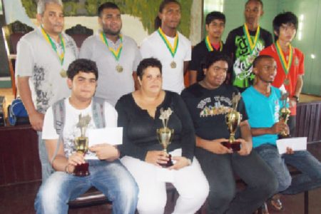 The winners of the Trophy Stall Chess Tournament display their trophies starting with, from left seated, Roberto Neto, Maria Thomas, Taffin Khan and Anthony Drayton. In the back row, from left, Raymond Singh, Ron Motilall, Carlos Petterson, Rajiv Muneshwer, Omar Britton-Grant and Haifeng Su.
