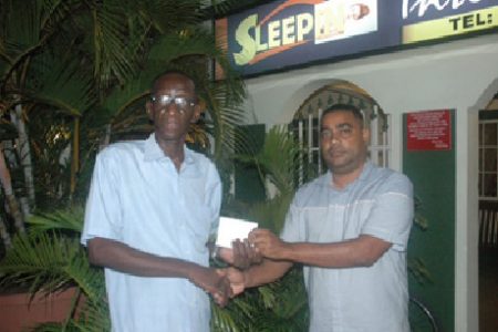 CEO of Sleepin International Hotel Clifton Bacchus (right) hands over the sponsorship cheque to Technical Delegate of the Boyce and Jefford Track & Field Classic IV Cornel Rose.