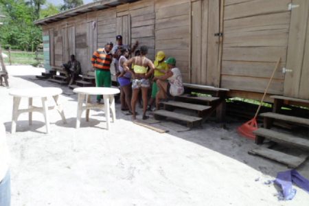 Some women of the 14 Miles back dam in discussion with GWMO President Simona Broomes in front of what is known as a ‘kaimoo,’ which is a crudely built structure with small rooms where women have sex with men for money.