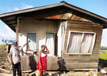 The couple stands in front of the house that was knocked off its pillars as Gershwyn Gordon points to the damaged front wall 