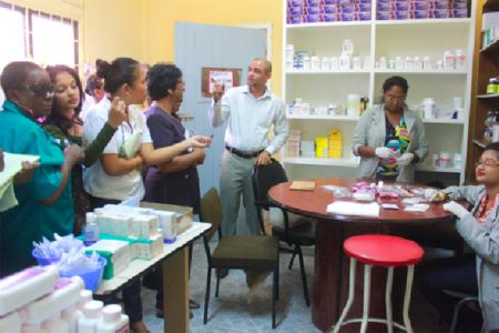 Hospital Director Kevin Mana speaking with members of the visiting Parliamentary Sector Committee on Social Services inside the pharmacy, where employees were busy at work packaging pills. (Photo by Arian Browne)