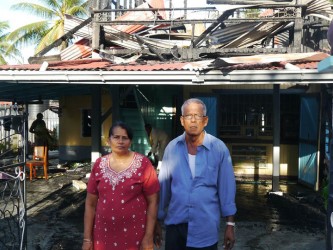 The couple stands in front of their burnt out house as relatives help to clean up (in the background) 