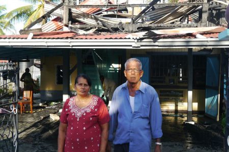 The couple stands in front of their burnt out house as relatives help to clean up (in the background)
