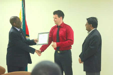 Bank of Guyana Governor Lawrence Williams (left) presents Creditinfo International Senior Manager Kristinn Örn Agnarsson with the licence while Finance Minister Dr Ashni Singh looks on
