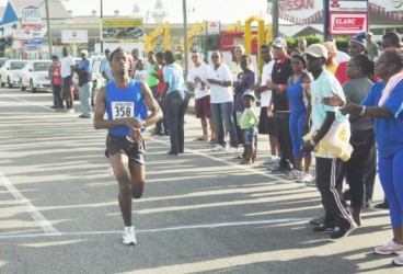 Cleveland Forde stops his watch after successfully defending his title yesterday morning at the Neal and Massy Group of Companies AinLim 10k road race. (Orlando Charles photo)